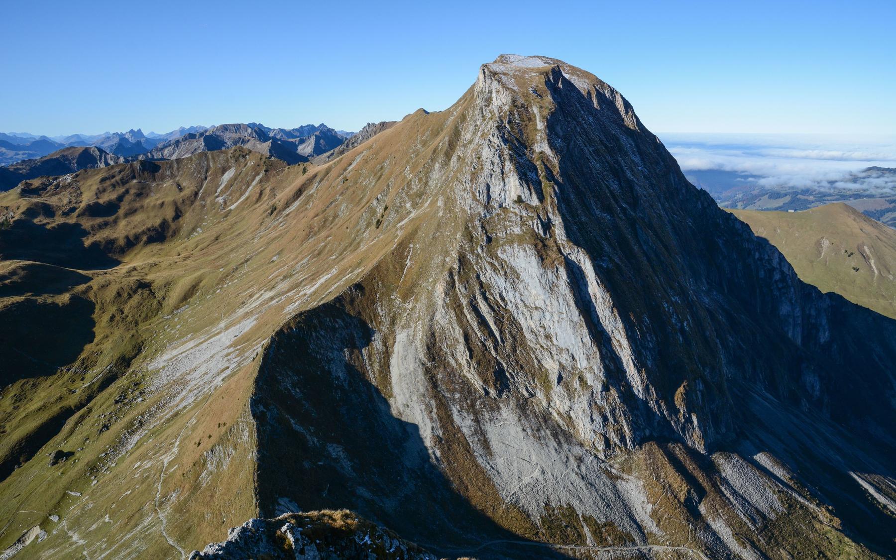 Overview: The Gantrisch seen from the Nüneneflue. Lower left the short ridge section over which the descent back to the Leiterepass (not visible anymore) is made. The branch from the hiking trail to the via ferrata can be seen on the lower right, the via ferrata runs through the sunny part of the rock face.